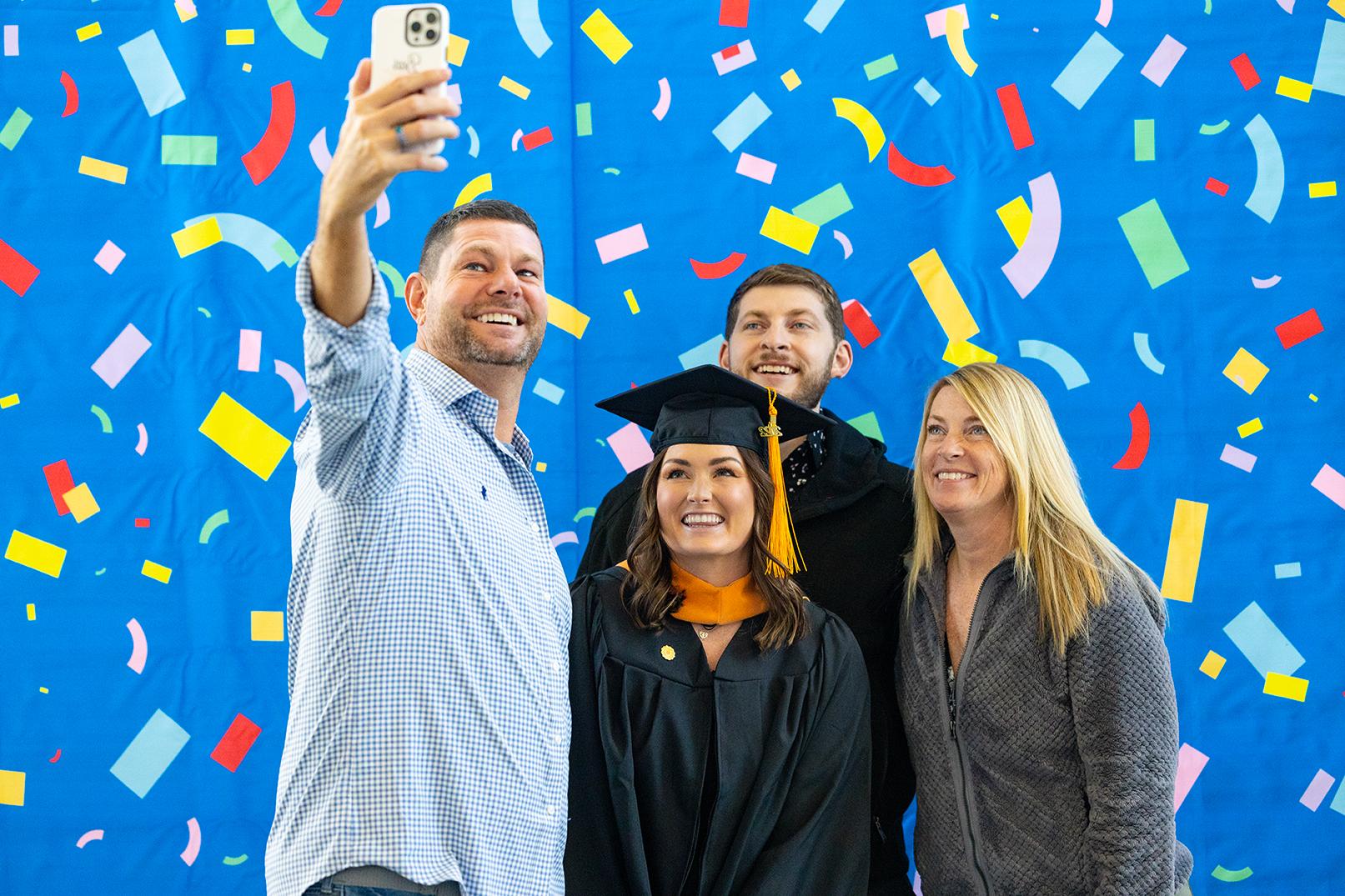 four people, taking a selfie in front of a backdrop