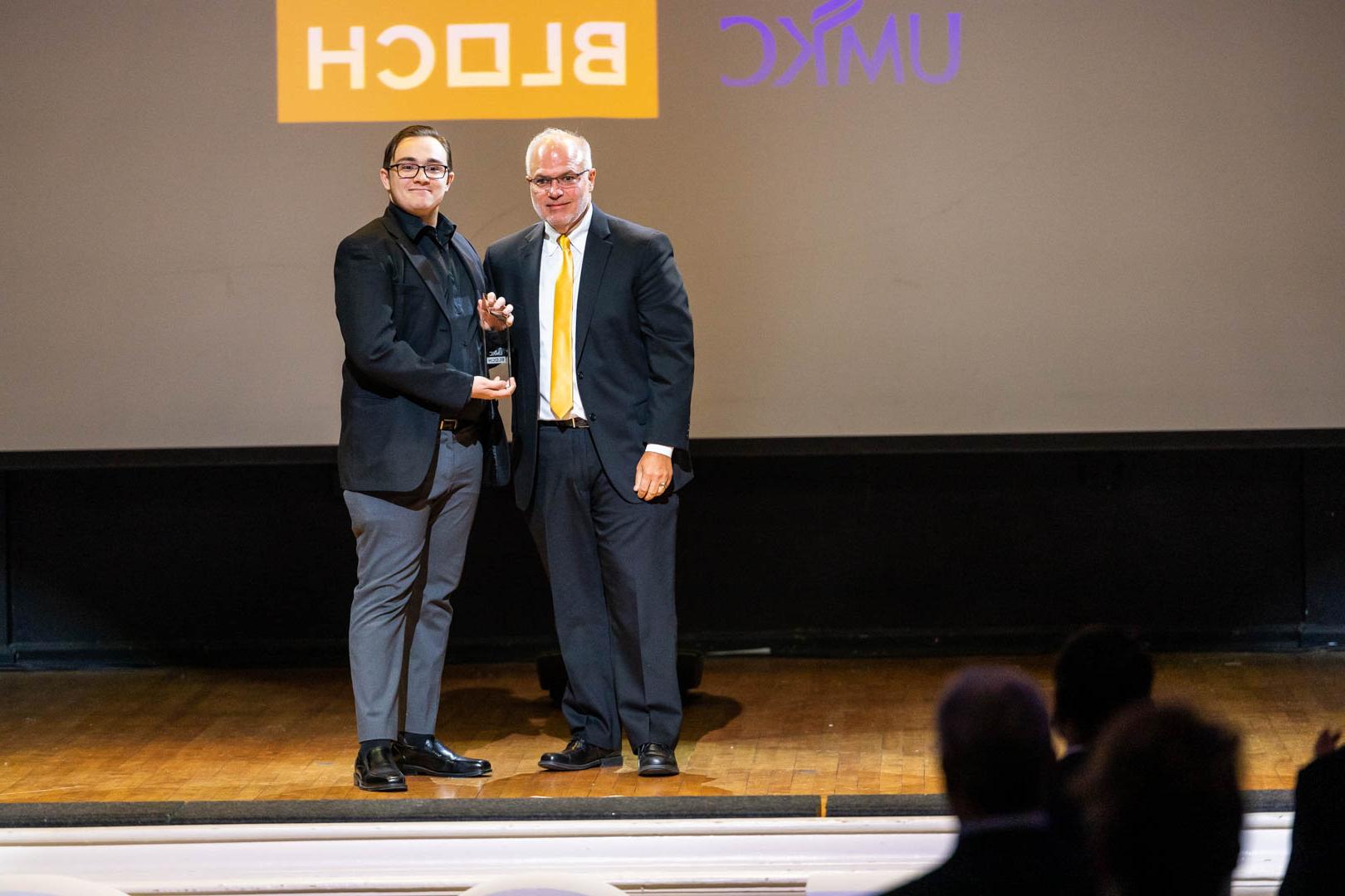a man presents a student with an award onstage